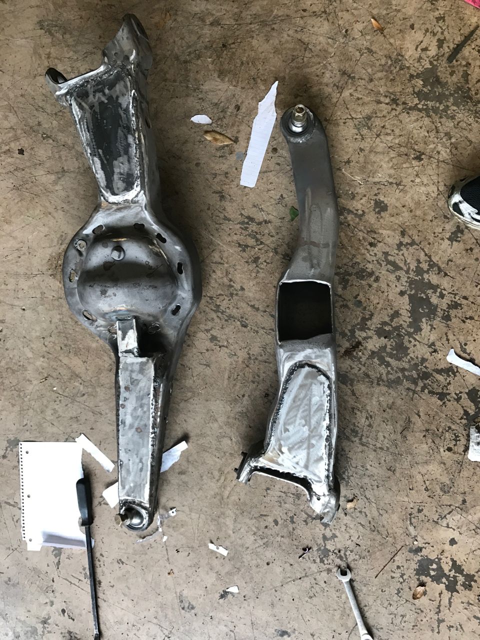 Two custom metal suspension parts for a vehicle on a concrete floor.
