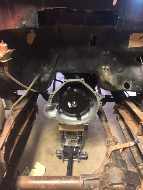 1982 Ford Bronco - A transmission bell housing is supported by a hydraulic jack and wooden blocks beneath a vehicle's frame. The drivetrain components, includ…