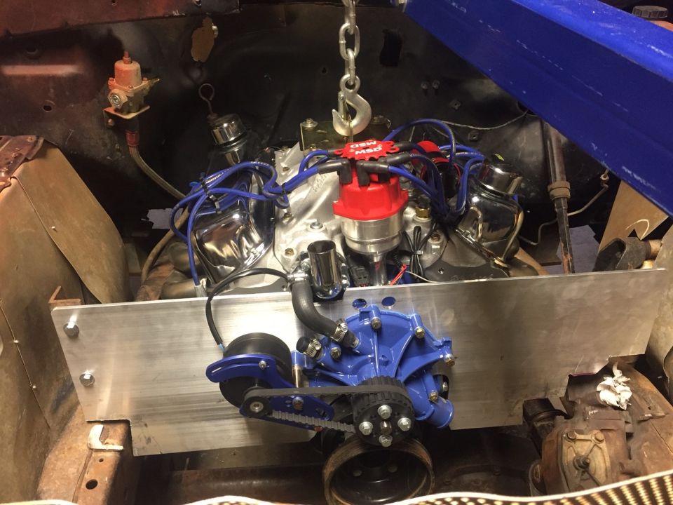 V8 engine installation with blue water pump and red MSD distributor, suspended by a chain.
