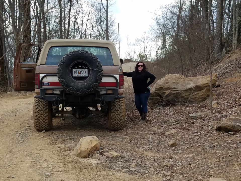 Woman standing next to a lifted tan and brown Ford Bronco with a spare tire on the rear.
