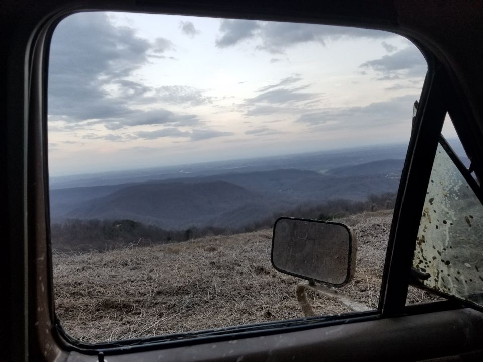 View from inside a vehicle looking out over mountains at dusk, with side mirror and dirty window.