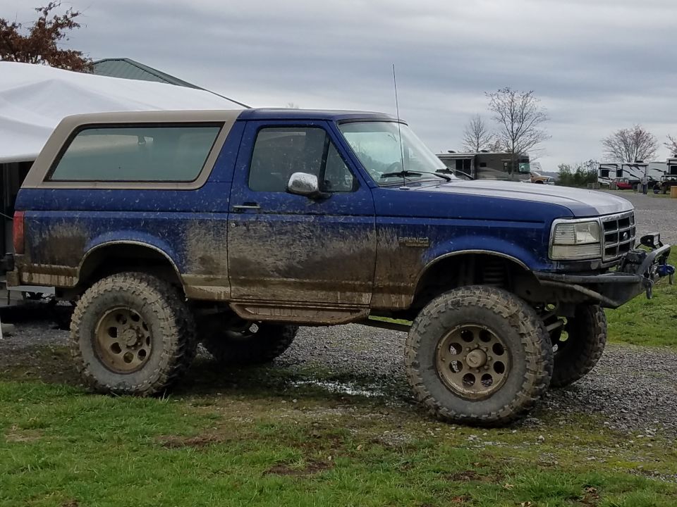 Muddy blue 1988 Ford Bronco with tan top and off-road tires.