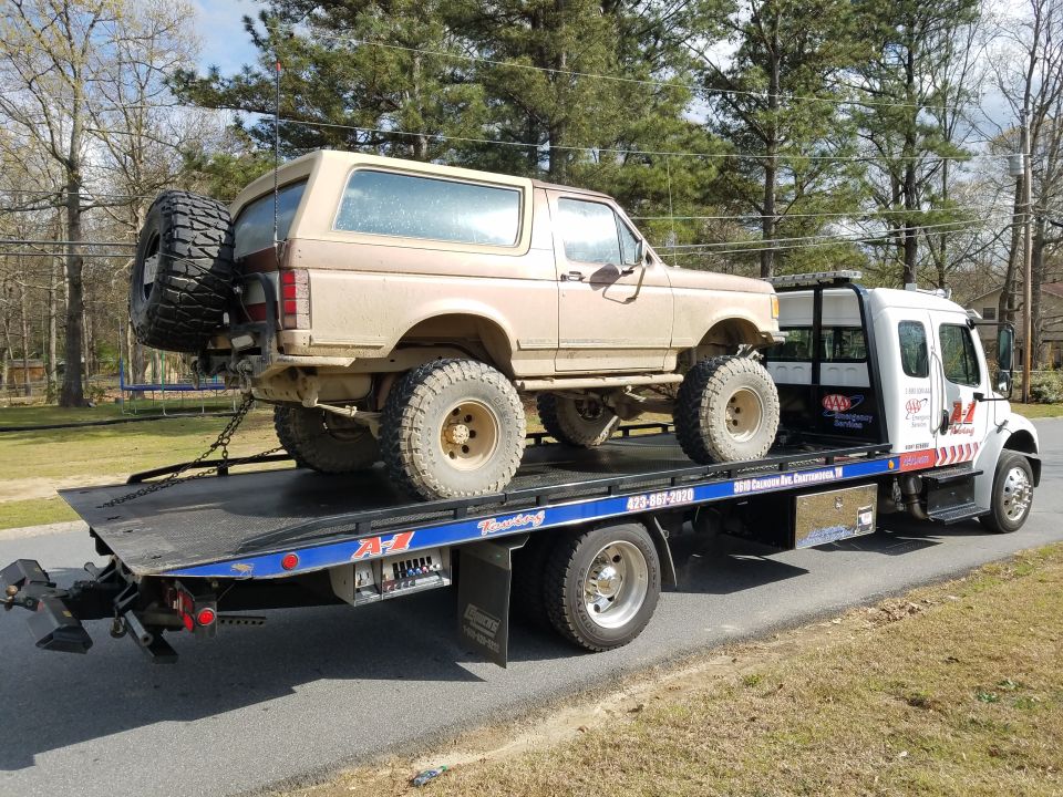Tan Ford Bronco on a flatbed tow truck with large off-road tires.