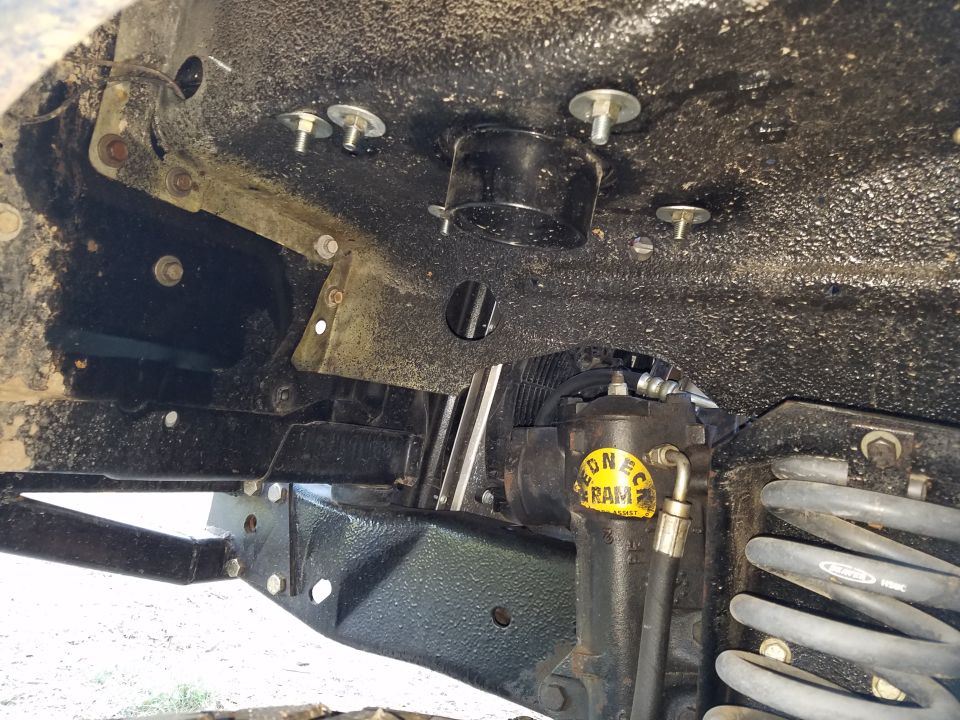 Underside of a vehicle showing steering ram assist, coil spring, and frame with bolts.