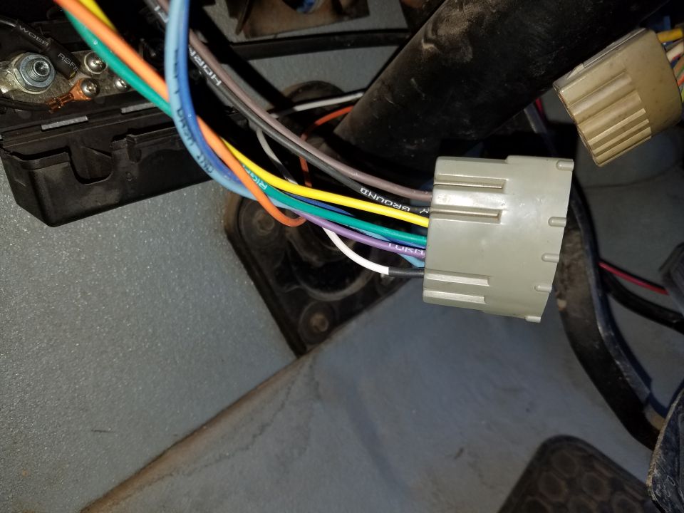 Automotive wiring harness connectors and wires, including a gray multi-pin connector and a black fuse box.