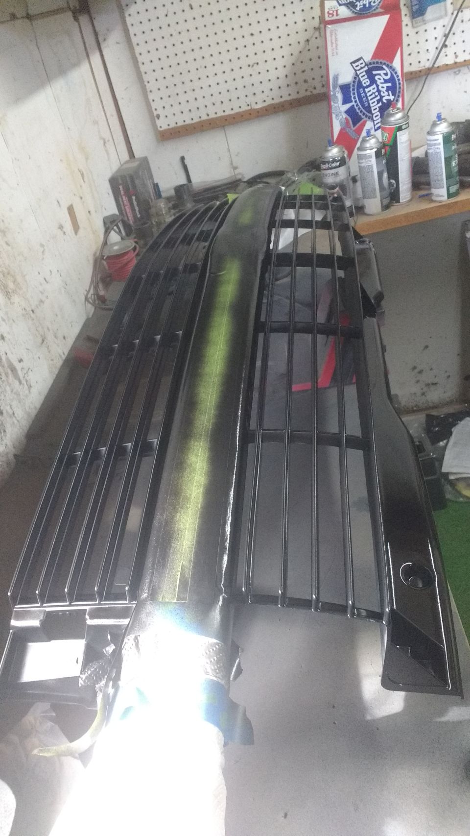 Black automotive grille with green spray paint accent, being worked on in a workshop.