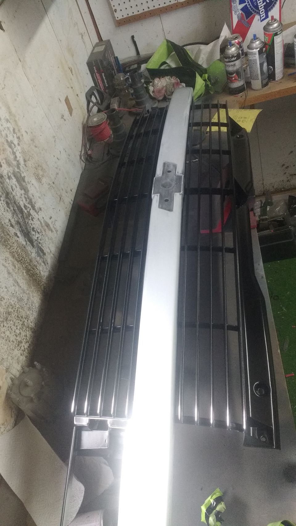 Two vehicle grilles, one chrome and one black, on a workbench.