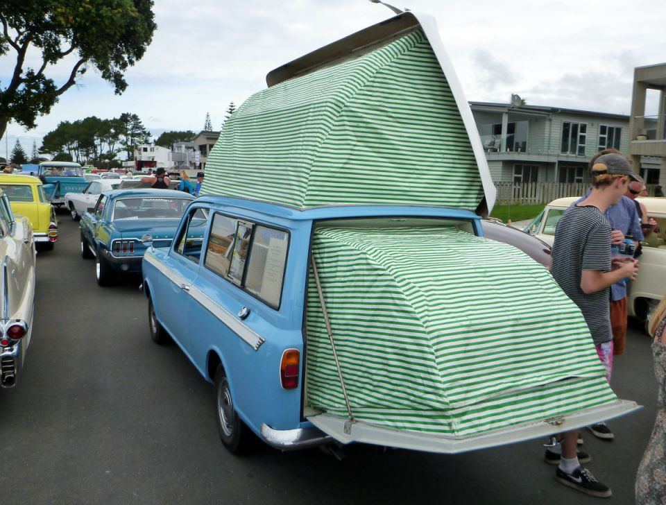 Light blue station wagon with green and white striped pop-top camper.