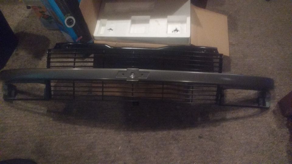 Two vehicle grilles, one black and one gray, on a carpeted floor.