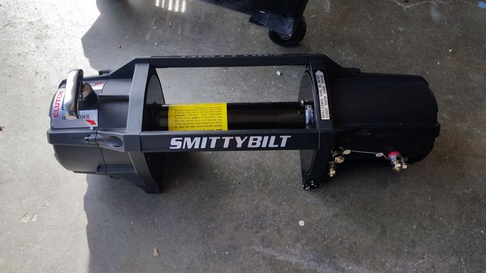 Black Smittybilt winch with silver clutch handle on concrete.