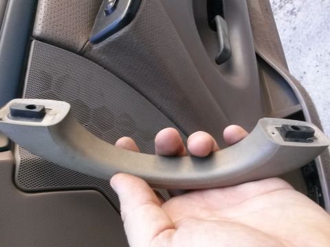 1996 Ford Bronco - A hand holds a tan interior door pull handle in front of a dark brown perforated door panel and speaker grille. The handle has black plasti…