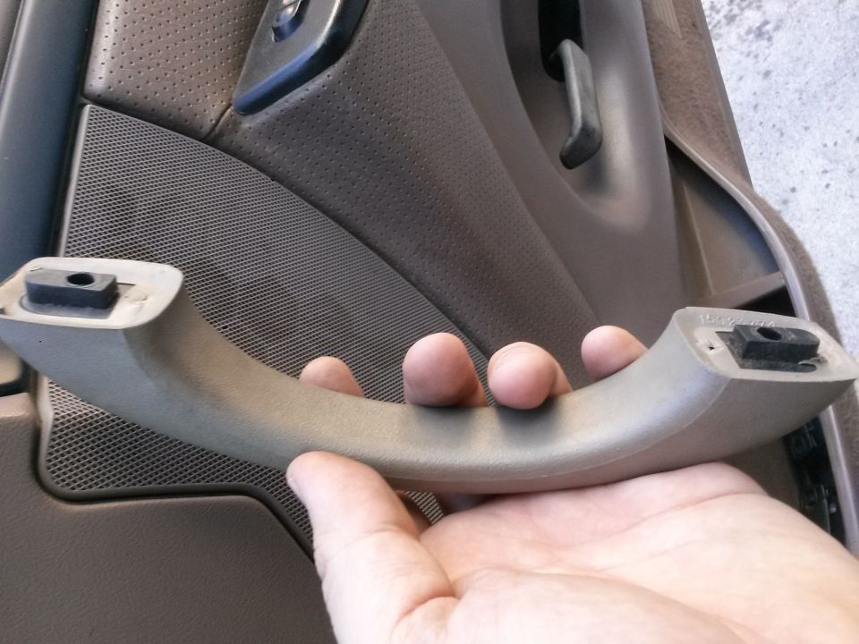 Hand holding a tan interior door pull handle against a car's door panel.