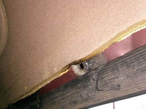 1996 Ford Bronco - A close-up view of the interior headliner of a vehicle, showing a hole in the insulation and a dark wooden trim piece below it.
