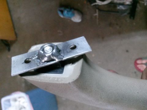 1996 Ford Bronco - A close-up shot shows a metal bracket with a nut and bolt welded onto a textured, curved plastic part, possibly a handle or trim piece.
