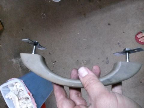 1996 Ford Bronco - A person's hands are holding a tan-colored interior grab handle with two metal mounting plates and screws attached to the ends. The backgro…