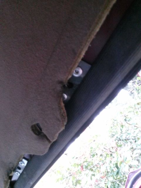 1996 Ford Bronco - Close-up view of the interior headliner of a vehicle, showing a metal bracket with screws attached to the frame. The headliner material is…