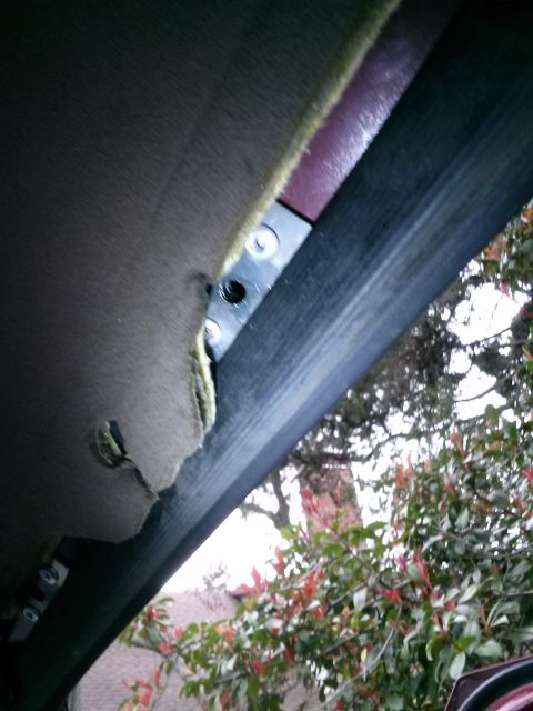 1996 Ford Bronco - A close-up view shows the underside of a vehicle's headliner that has been pulled back, revealing a metal bracket secured with screws. The…