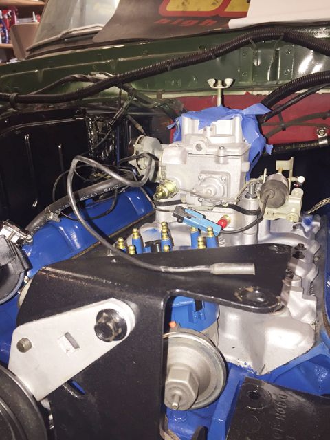 1978 Ford Bronco - A close-up view of a V8 engine bay, featuring a carburetor with blue tape, spark plug wires, and a black metal bracket. The engine block an…