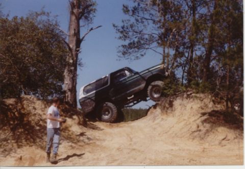 1995 Ford Bronco - A Ford Bronco navigates a steep dirt incline, its front-left wheel lifted off the ground.