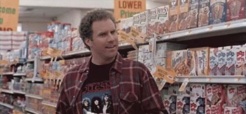 1995 Mercury Grand Marquis - A man wearing a plaid shirt over a band t-shirt stands in an aisle of a grocery store, looking to his right. The shelves are stocked with v…