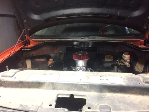 1982 Ford Bronco - The open hood of a vehicle reveals a partially assembled engine bay. A red air filter sits atop a carburetor, with a brake fluid reservoir…