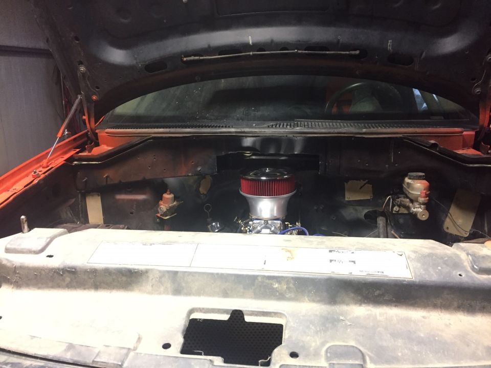 Vehicle engine bay with red air filter and carburetor.