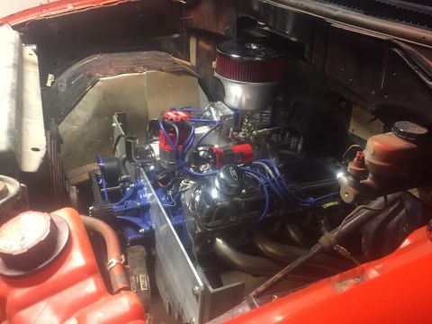 1982 Ford Bronco - A custom engine is installed in the engine bay of a red vehicle, likely a truck or SUV. The engine features a chrome air cleaner, blue spar…