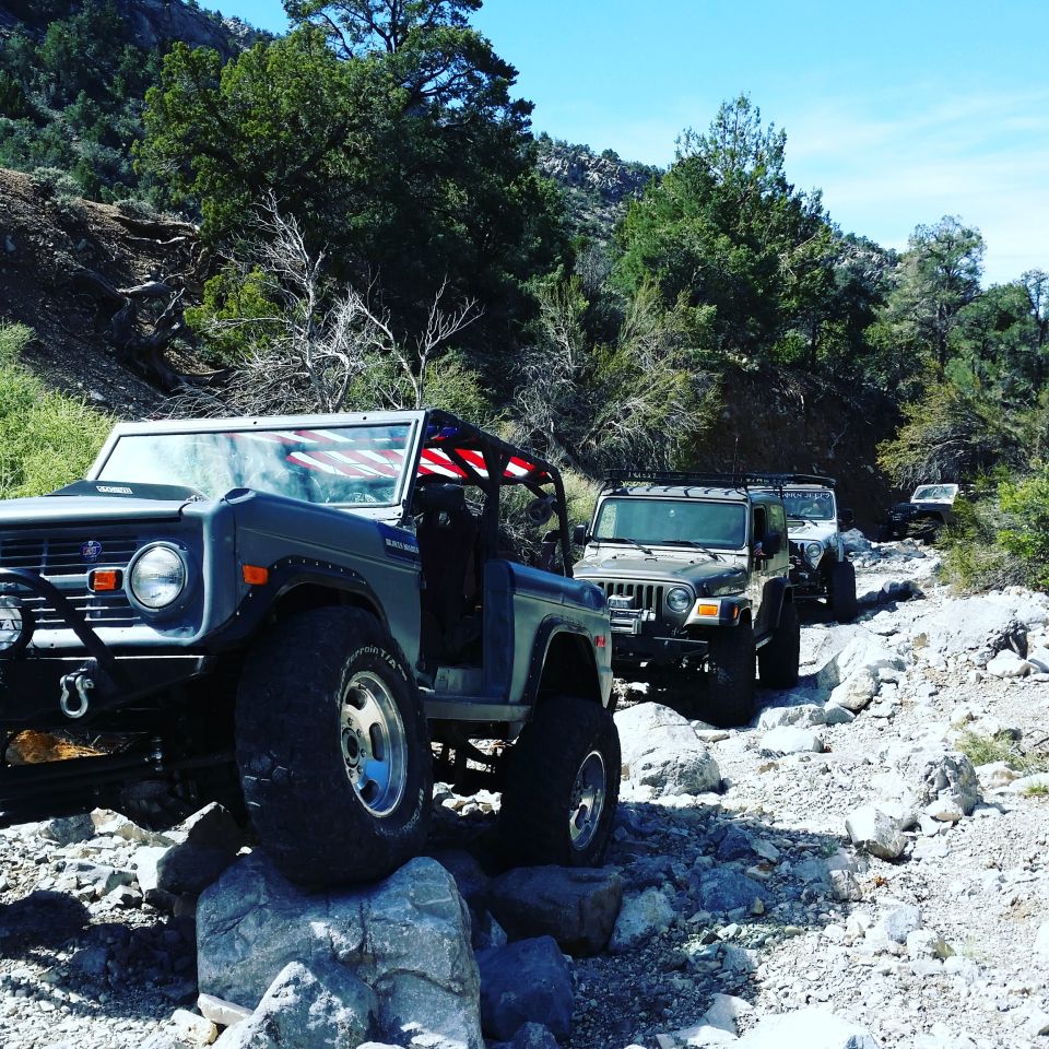 Off-road vehicles on a rocky trail, led by a Ford Bronco with an American flag.