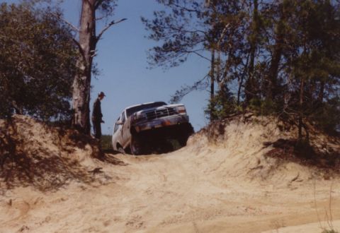 1995 Ford Bronco - Scanned photo of a lifted 1990s Ford Bronco cresting the lip of a sand hill on a rutted trail, its front end tipped up against a blue sky w…