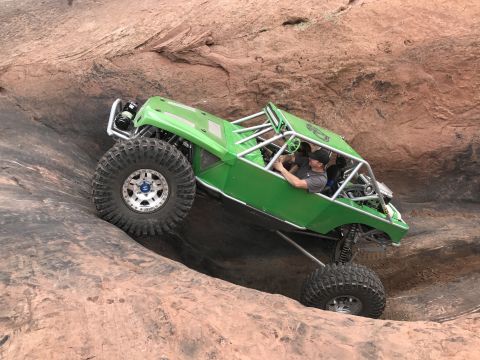 1991 Ford Bronco - A bright green custom off-road buggy with large tires navigates a steep, rocky incline. The driver, wearing a black baseball cap, is visibl…
