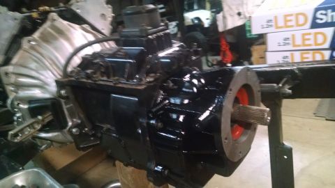 1985 Jeep CJ7 - A close-up, low-angle view of a black transmission assembly with a silver transfer case attached. The output shaft of the transmission is v…