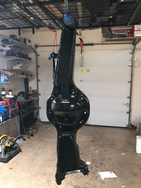 1996 Ford Bronco - A black painted rear axle housing is suspended by chains in a garage. The housing has a round differential cover bolted to it and appears t…