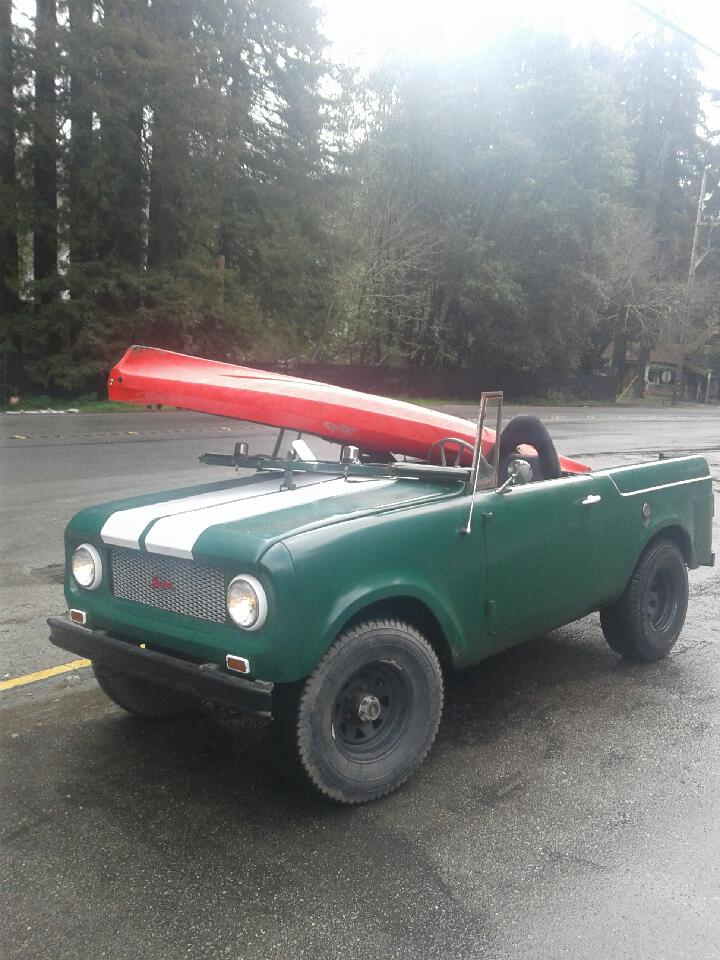 Green International Harvester Scout II with a red canoe on top, parked on a wet road.