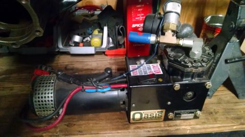 1985 Jeep CJ7 - A black Oasis brand air compressor unit with red and blue wires is mounted on a wooden surface, with various tools and parts in the backgro…