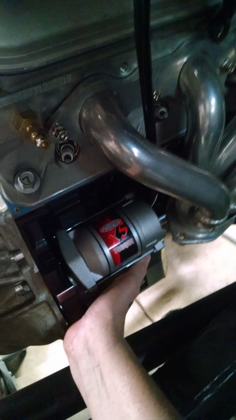 1985 Jeep CJ7 - A hand is shown holding a Powermaster XS Torque starter motor, which is installed on an engine. Exhaust headers and part of the engine bloc…