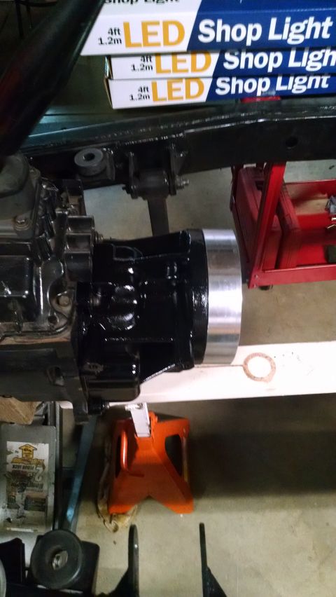 1985 Jeep CJ7 - A black transmission assembly with a silver-banded output shaft is mounted beneath a vehicle frame. Several boxes of LED shop lights are st…