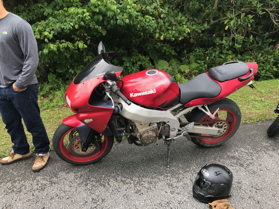 Red Kawasaki sport motorcycle parked on roadside with helmet on ground