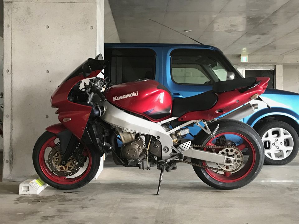Red and silver Kawasaki sportbike parked next to a blue car.