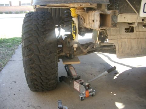 1994 Ford Bronco - Close-up of a vehicle's front suspension and tire, supported by a jack and wooden block.