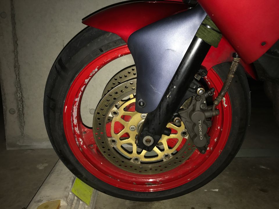 Motorcycle front wheel with red rim, gold brake rotor, and Tokico caliper.