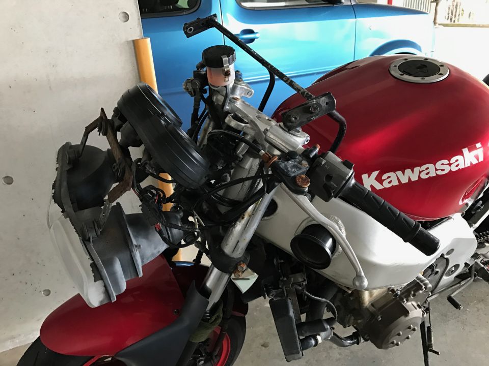Partially disassembled red Kawasaki motorcycle with fairing removed, exposing headlight and wiring, in a garage
