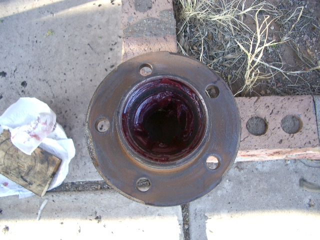 Greased wheel hub assembly with five bolt holes, resting on concrete and bricks