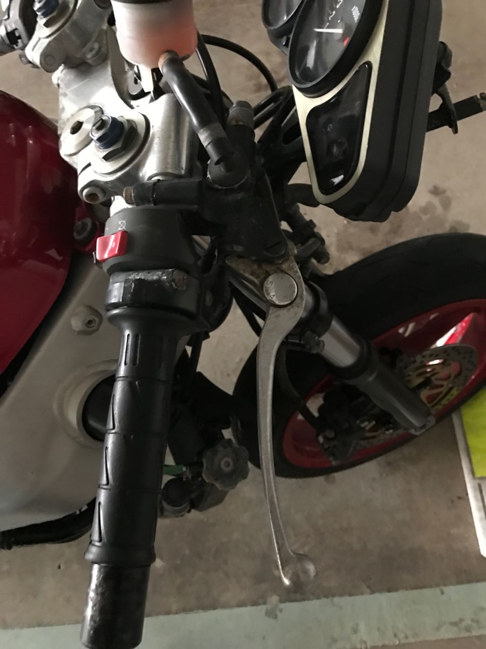 Close-up of red motorcycle handlebars, brake lever, and front fork.