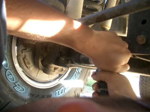 1994 Ford Bronco - Hands work on the suspension components near the tire of a vehicle.