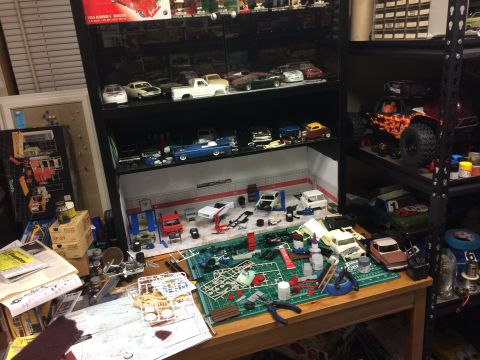 1989 Ford Bronco - A cluttered workbench displays a model car garage diorama, unassembled kits, and tools.