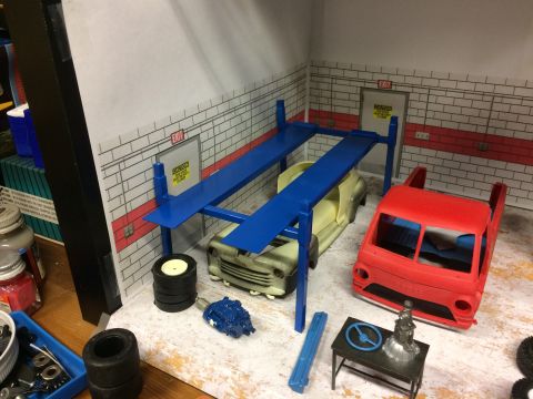 1989 Ford Bronco - A model car garage diorama features a car on a lift, a red truck, and various automotive parts scattered around.
