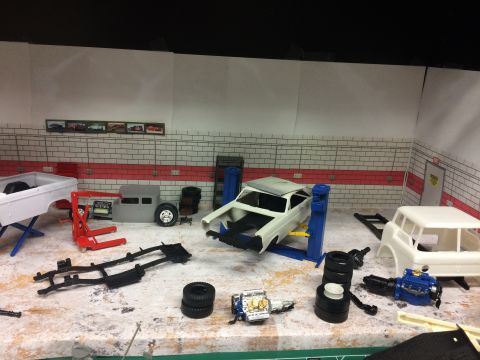 1989 Ford Bronco - A diorama depicts a model car garage with various unassembled vehicle parts and a car body on a lift.