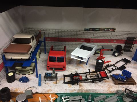 1989 Ford Bronco - A diorama depicts a model car garage scene with various unfinished vehicle models and parts scattered around.