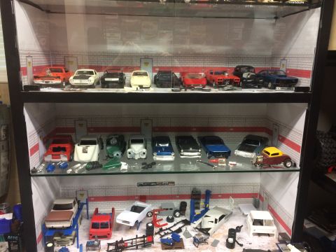 1989 Ford Bronco - A collection of model cars and automotive parts are displayed in a multi-tiered cabinet.
