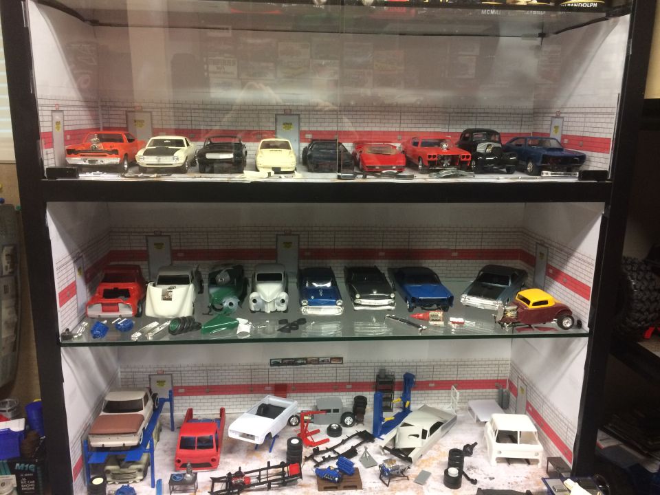 Display case filled with model cars and parts, some on lifts
